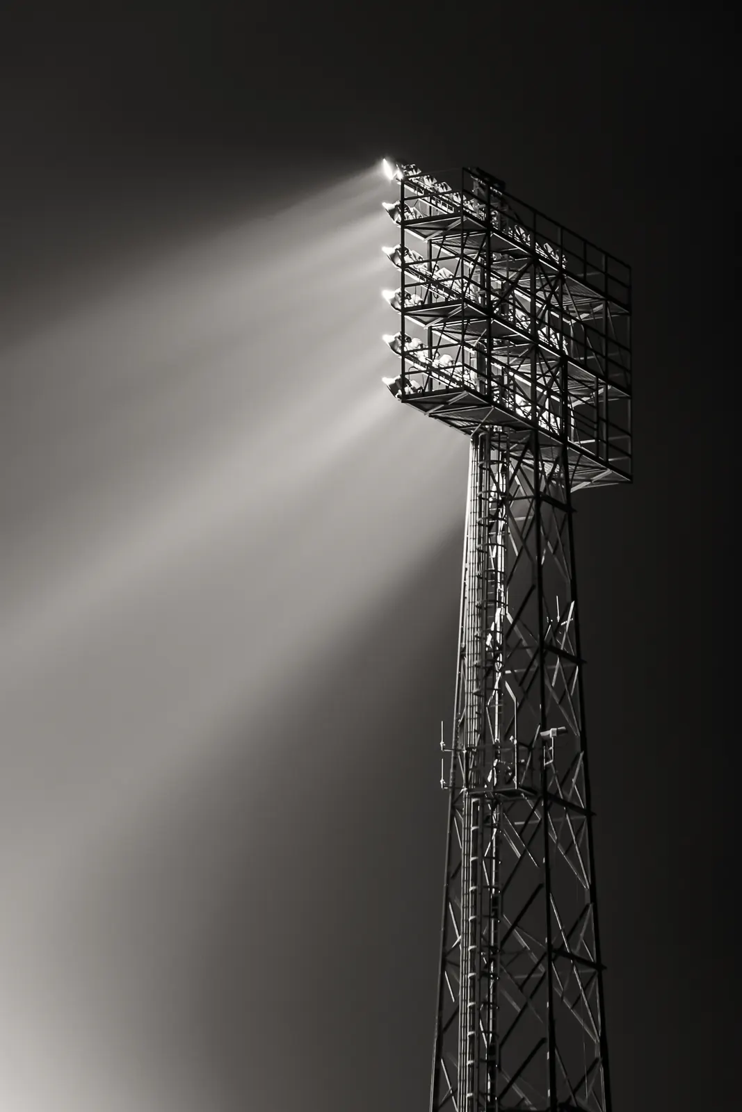 Zwart-witfoto van een stadionlichtmast waarvan het licht door de mist schijnt